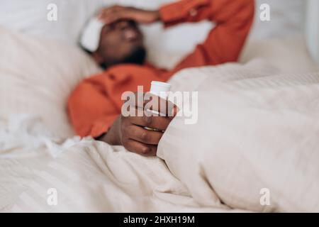 Jeune Afro-américain en chemise orange avec patch sur le front souffre de la haute température de repos dans le grand lit vue latérale Banque D'Images