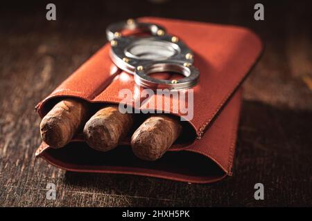 Trois cigares et un cutter dans un contenant en cuir sur une table en bois Banque D'Images