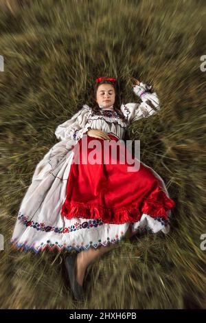 Salaj, Roumanie - 15 mai 2018 : jeune fille rurale vêtue de costumes traditionnels assis dans un hanyloft au moment de la récolte à la campagne Banque D'Images