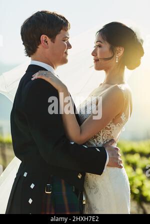 Maintenant et pour toujours mon cher. Photo d'une jeune mariée et d'un marié joyeux se tenant les uns les autres tout en regardant l'extérieur de l'œil à l'œil pendant la journée. Banque D'Images