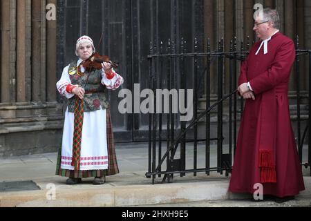 Un musicien au violon, vêtu d'une robe nationale lituanienne, joue des chansons lituaniennes et ukrainiennes regardées par le vice-doyen de la cathédrale de Peterborough Tim Alban Jones. À une époque où l'Ukraine est attaquée par la Russie de Vladimir Poutine, les Lituaniens célèbrent leur restauration le jour de l'indépendance à la cathédrale de Peterborough. Ils soutiennent l'Ukraine et tiennent les drapeaux et rubans ukrainiens. La Lituanie a retrouvé sa liberté de l'Union soviétique le 11th 1990 mars. Une courte prière et un silence d'une minute ont été organisés pour les défenseurs de la liberté déchus. Banque D'Images