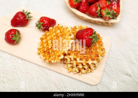 Gaufres servies avec des fraises sur une planche à découper blanche sur une table grise et un panier de fraises mûres Banque D'Images