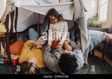 Bonne petite fille jouant avec sa mère et son père à la maison. Adorable petite fille riant gaiement tout en étant assise sur son père. Famille de trois Banque D'Images