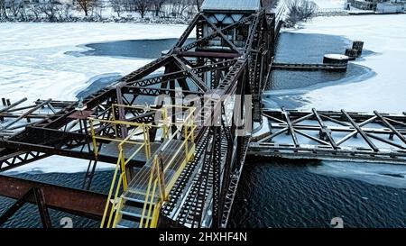 C'est tôt le matin avec de la neige tombant sur l'ancienne passerelle rouillée au-dessus du pont tournant de chemin de fer. Banque D'Images