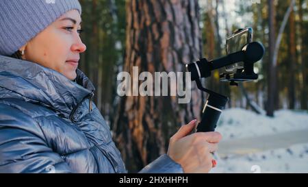 La femme vidéaste professionnelle tenant un smartphone sur le dispositif de stabilisation de nacelle 3 axes en hiver.Pro Equipment permet de réaliser des vidéos de haute qualité Banque D'Images