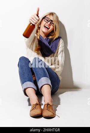 Vivez la fête, aimez la fête, soyez la fête. Portrait en studio complet d'une jeune femme ayant une bière tout en s'appuyant contre un mur. Banque D'Images