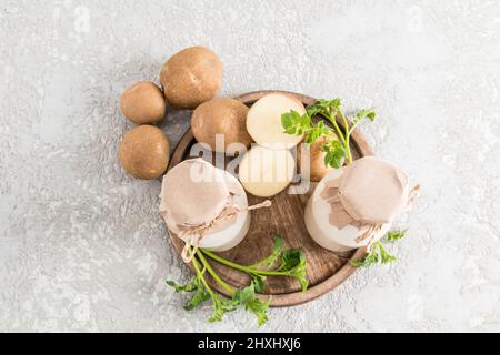 vue de dessus de deux bouteilles de verre avec du lait de pomme de terre végétale et des tubercules de pomme de terre hachés sur un plateau en bois fond de béton gris Banque D'Images