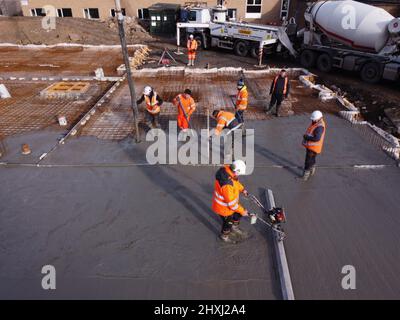 Les ouvriers sur place à la construction de la maison, versant la couche de béton de base d'un mélangeur via une pompe hydraulique Banque D'Images