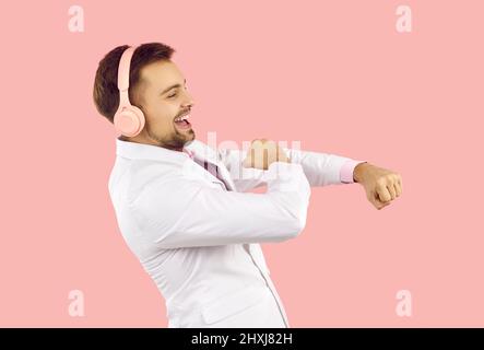 Joyeux homme s'amusant et dansant à la musique qu'il écoute dans des écouteurs sur fond rose. Banque D'Images