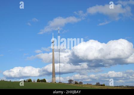 Deux grands mâts d'émetteur bas nuages blancs dans le ciel bleu et le champ vert Banque D'Images