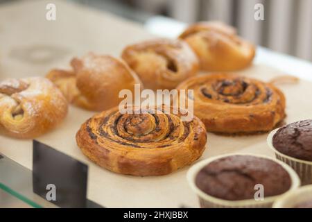 Variété de muffins et petits pains cuits dans un verre vitrine au café de boulangerie. Beignets et anneaux. Des pâtisseries chaudes se trouvent sur l'étagère du café. Petits pains et muffins au chocolat Banque D'Images