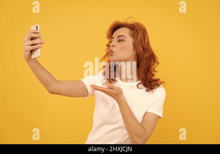 Femme faire la main embrasser geste à l'appareil photo téléphone mobile fond jaune, selfie Banque D'Images