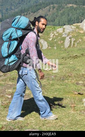 Vue latérale d'un homme qui regarde l'appareil photo tout en marchant sur la montagne avec un sac à dos en parachute Banque D'Images
