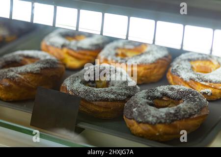 Divers gâteaux de crème anglaise cuits dans une vitrine en verre au café de la boulangerie. Beignets et anneaux. Des pâtisseries chaudes se trouvent sur l'étagère du café. Banque D'Images
