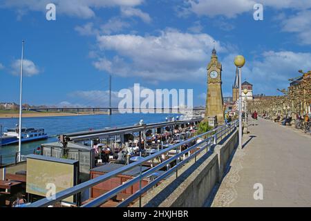 Düsseldorf (Rheinpromenade), Allemagne - mars 9. 2022: Vue sur la promenade du bord du rhin avec des cafés-restaurants sur la tour de l'horloge contre le ciel bleu Banque D'Images