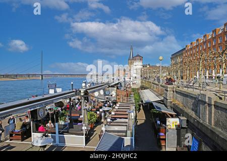 Düsseldorf (Rheinpromenade), Allemagne - mars 9. 2022: Vue sur la promenade au bord de la rivière, cafés-restaurants en plein air avec ciel bleu d'hiver sur le château médiéval Banque D'Images