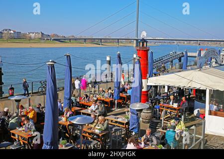 Düsseldorf (Rheinpromenade), Allemagne - mars 9. 2022: Vue sur le restaurant extérieur, les gens assis le jour d'hiver ensoleillé, pont Oberkasseler fleuve rhin Banque D'Images