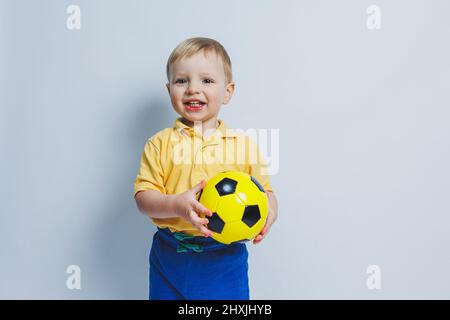 Un petit garçon avec un ballon de football dans ses mains sur fond blanc, un enfant est un joueur de football débutant, un sport pour les enfants. Petit athlète. Jaune Banque D'Images