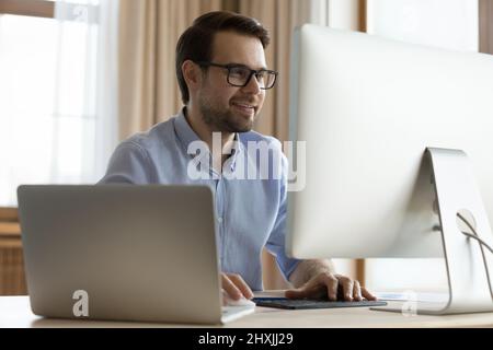 Jeune homme souriant développeur de logiciels utilisant deux ordinateurs au travail Banque D'Images