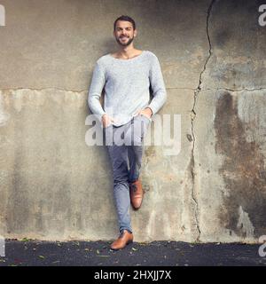 Style inspiré par la ville. Photo d'un beau jeune homme posant contre un mur urbain. Banque D'Images