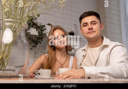Heureux couple assis au portrait de cuisine. Belle femme et beau homme qui boit du thé ou du café. Concept de relations d'appel d'offres. Photo de haute qualité Banque D'Images
