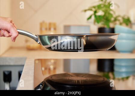 Une femme tient une poêle en acier sur une cuisinière à induction dans la cuisine, un appareil de cuisine moderne Banque D'Images