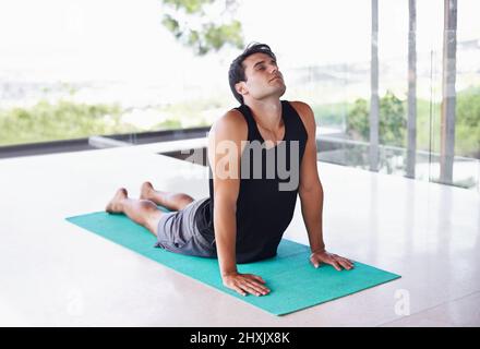 Seulement l'énergie positive ici. Un jeune homme content faisant du yoga à la maison. Banque D'Images