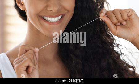 Soins buccaux. Gros plan de la jeune femme souriante à l'aide de la soie dentaire Banque D'Images