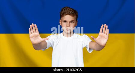 Un adolescent fait un geste d'arrêt sur fond de drapeau ukrainien bleu jaune Banque D'Images