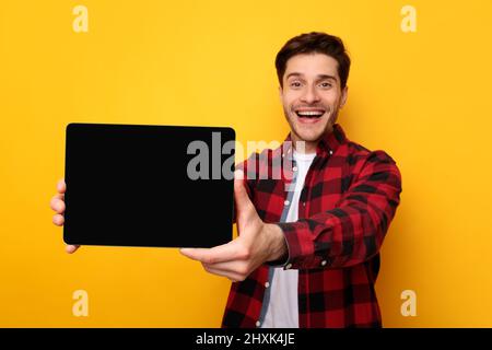 Jeune homme heureux montrant un écran vide noir de tablette Banque D'Images