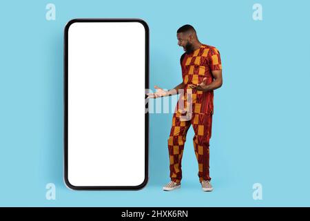 Offre incroyable. Black Man surpris en costume traditionnel regardant le smartphone vierge Banque D'Images