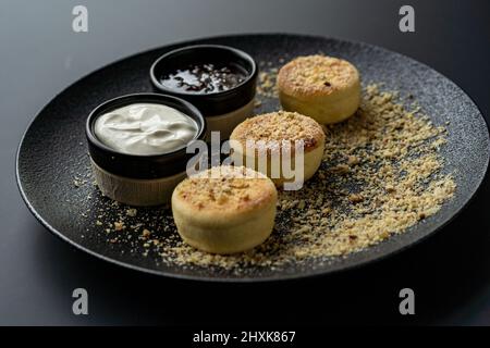 cheesecake au fromage cottage dans une assiette noire avec de la crème aigre et de la confiture Banque D'Images