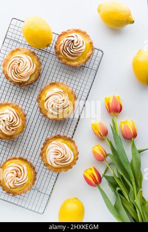 De délicieuses tartelettes au citron meringue maison, avec des tulipes sur le côté. Banque D'Images