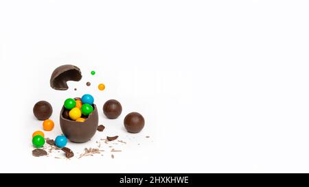 Œuf de pâques au chocolat craqué avec de petites friandises rondes colorées et des chocolats sur fond blanc, espace de copie, bannière. Un œuf de chocolat au lait cassé avec Banque D'Images