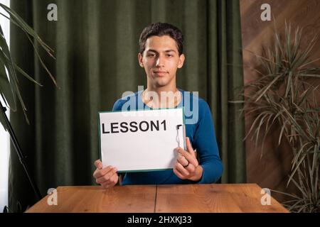 Souriant jeune homme d'affaires arabe assis à la table, parlant sur webcam avec appel vidéo ou chat avec le client, causerie, tournage tutoriel en ligne, enregistrement Banque D'Images