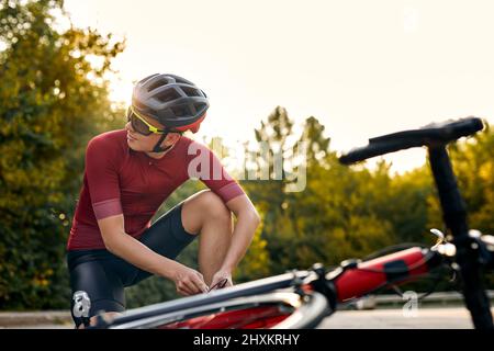 Homme ayant arrêté, étant à l'extérieur, fixant vélo par ses propres forces, changeant les détails, des problèmes de mouvement, athlète sportif caucasien portant sportif Banque D'Images