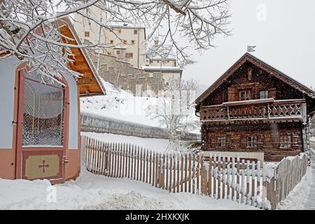 Petite ancienne maison en bois avec clôture en bois et chapelle en premier plan, arrière-plan fortressin tous couverts de neige, Mauterndorf, Autriche Banque D'Images