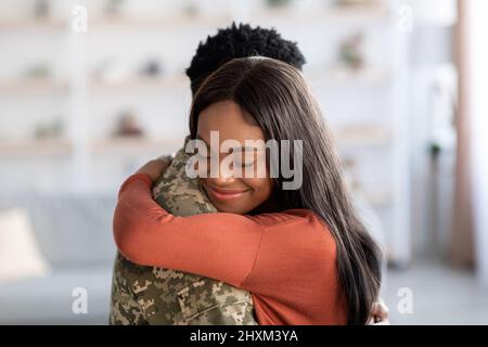 Concept de la Réunion. Belle femme noire heureuse embrassant mari militaire à la maison Banque D'Images