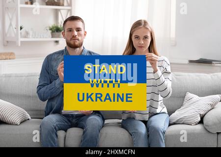 Jeune couple patriotique tenant une affiche avec Stand avec l'inscription de l'Ukraine Banque D'Images