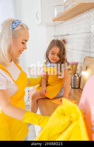 Une maman caucasienne souriante enseignant les filles essuyant la table dans la cuisine après la cuisson Banque D'Images