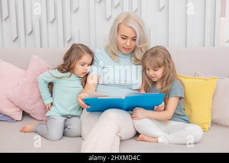 Une maman caucasienne souriante enseignant les filles assises sur le canapé dans le salon. Concept de famille heureux. Banque D'Images