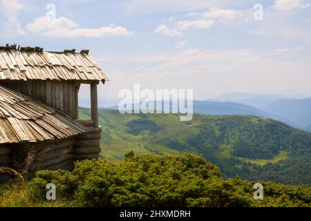 Paysage de montagne en soirée d'été avec abri touristique ancien abandonné sur des collines herbeuses et des sommets lointains au coucher du soleil coloré. Banque D'Images