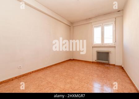 chambre vide avec sol en grès orange, radiateur en fer forgé et fenêtre en aluminium blanc Banque D'Images