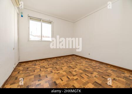 chambre vide avec sol en bois de type sintasol, murs peints en blanc, climatisation et fenêtre en aluminium avec volet Banque D'Images