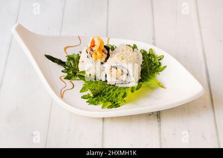 Tempura Maki Sushi - rouleau de viande de crabe, de paprika et de laitue à l'intérieur. Servi sur une feuille de shiso et une petite assiette blanche en forme de feuille Banque D'Images