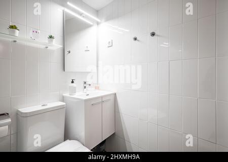 Salle de bains avec armoires en bois blanc, douche à parois de verre et miroir carré au-dessus du lavabo dans l'appartement de location de vacances Banque D'Images