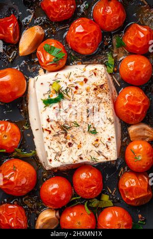 Fromage feta cuit au four avec tomates cerises et herbes en gros plan. Vue de dessus. Préparation de la pâte feta. Banque D'Images