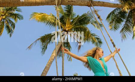 Jolie femme balançant sur une balançoire sur une plage tropicale, sur les rives de la mer turquoise. Concept voyage, promenades, repos dans la mer, tropical Resort côte détente voyage tourisme vacances d'été Banque D'Images