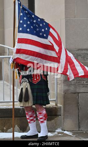 Wilkes barre, États-Unis. 13th mars 2022. Un tambour majeur pour une équipe de cornemuses débarque le drapeau américain avant de se mettre en place pour mars dans la parade de Saint Patrick. La tempête d'hiver de samedi a laissé 5 pouces de neige, mais la parade de Saint Patrick dans le centre-ville de Wilkes-barre a eu lieu dimanche. Les employés de la ville ont débarraché les rues tard le samedi et tôt le dimanche. La température de la parade ne l'a jamais fait au-dessus de 30 degrés. Crédit : SOPA Images Limited/Alamy Live News Banque D'Images