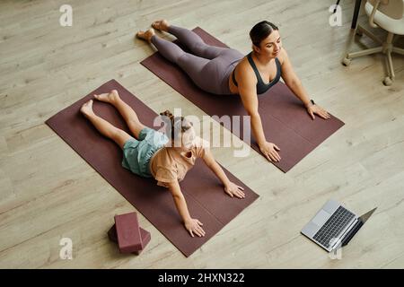 Vue de dessus de la mère et de la fille avec le syndrome de Down s'exerçant ensemble à la maison et faisant des exercices d'étirement sur les tapis tout en regardant la leçon en ligne Banque D'Images